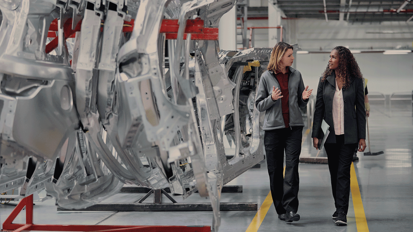 Two people walking and talking in a auto factory